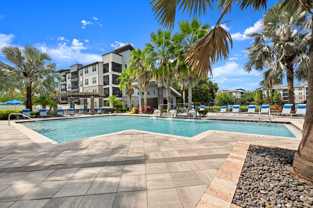 a swimming pool with palm trees and buildings in the background at Pavilion Luxury Apartments, Riverview, FL, Florida