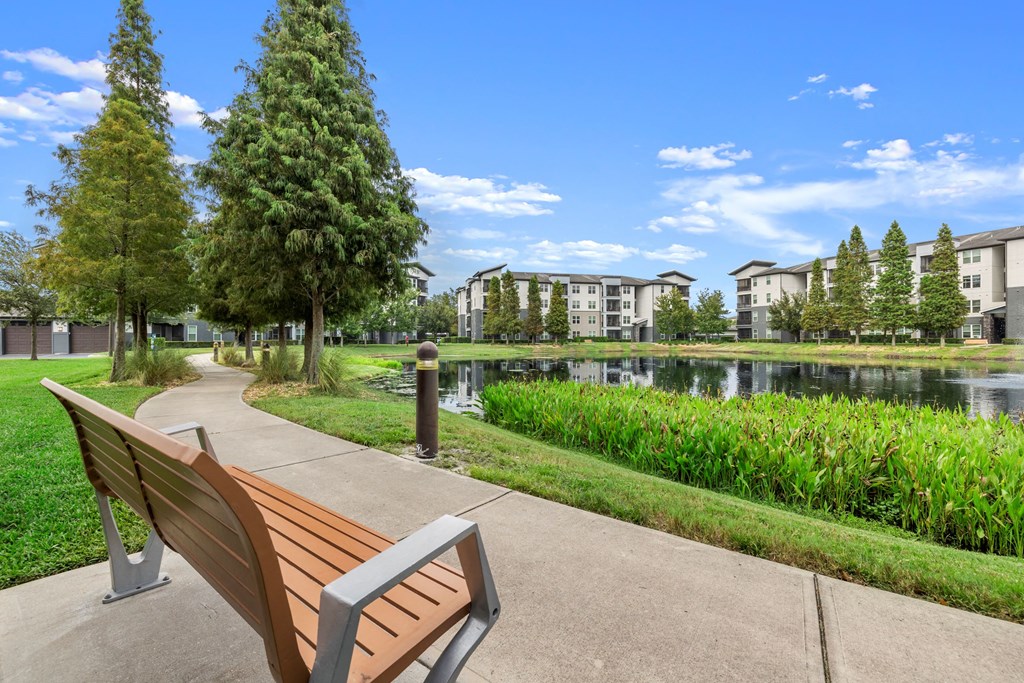 a park bench overlooking a lake with apartment buildings in the background at Pearce at Pavilion Luxury Apartments, Riverview, Florida