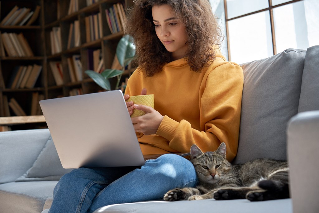 a woman sitting on a couch with a cat and a laptop