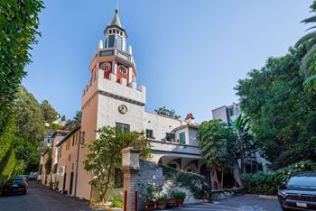 A white building with a tower has a red window on the second floor.