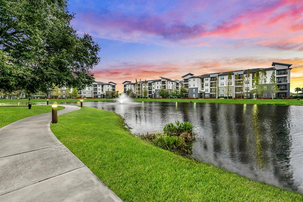 a sidewalk next to a lake with a fountain at Pearce at Pavilion Luxury Apartments, Riverview, Florida