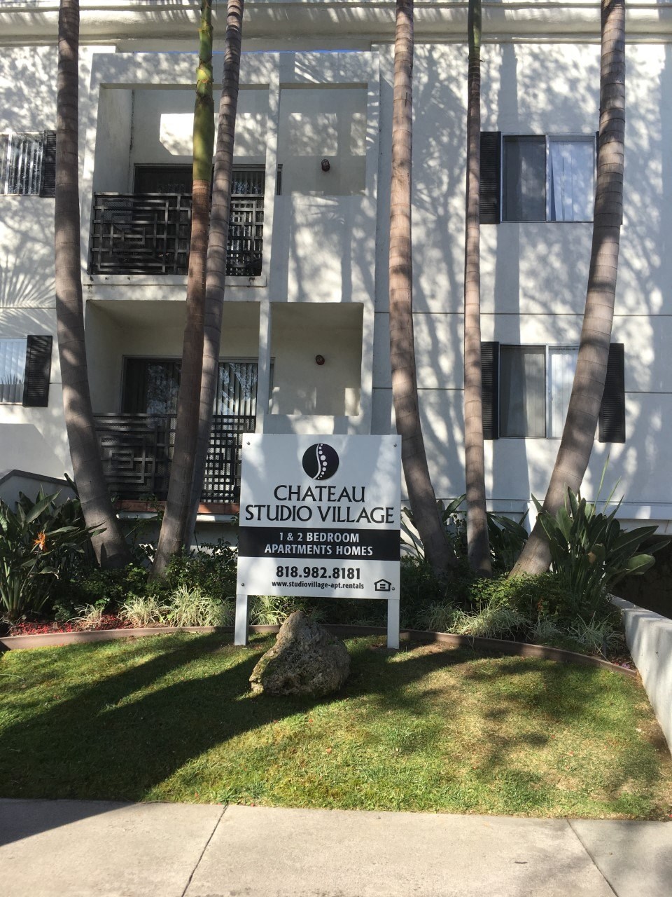 A sign for Chateau Studio Village stands in front of a white building with balconies.