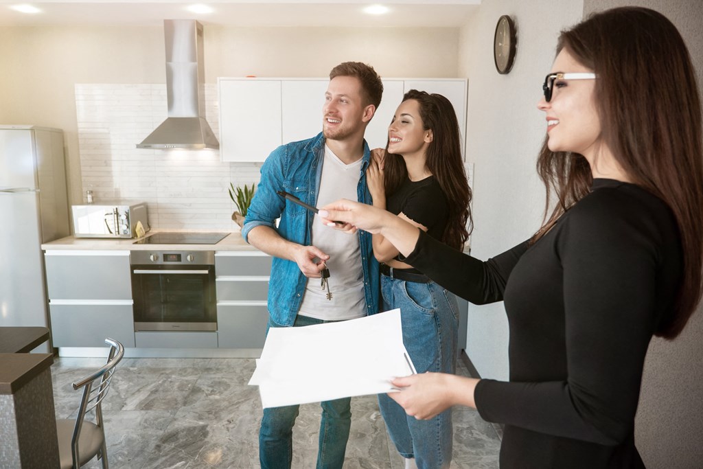 three people standing in a kitchen talking to a woman holding a document