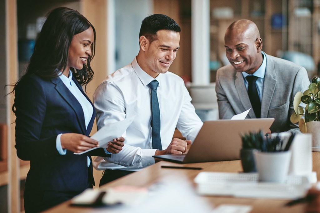 three people in an office looking at a laptop computer