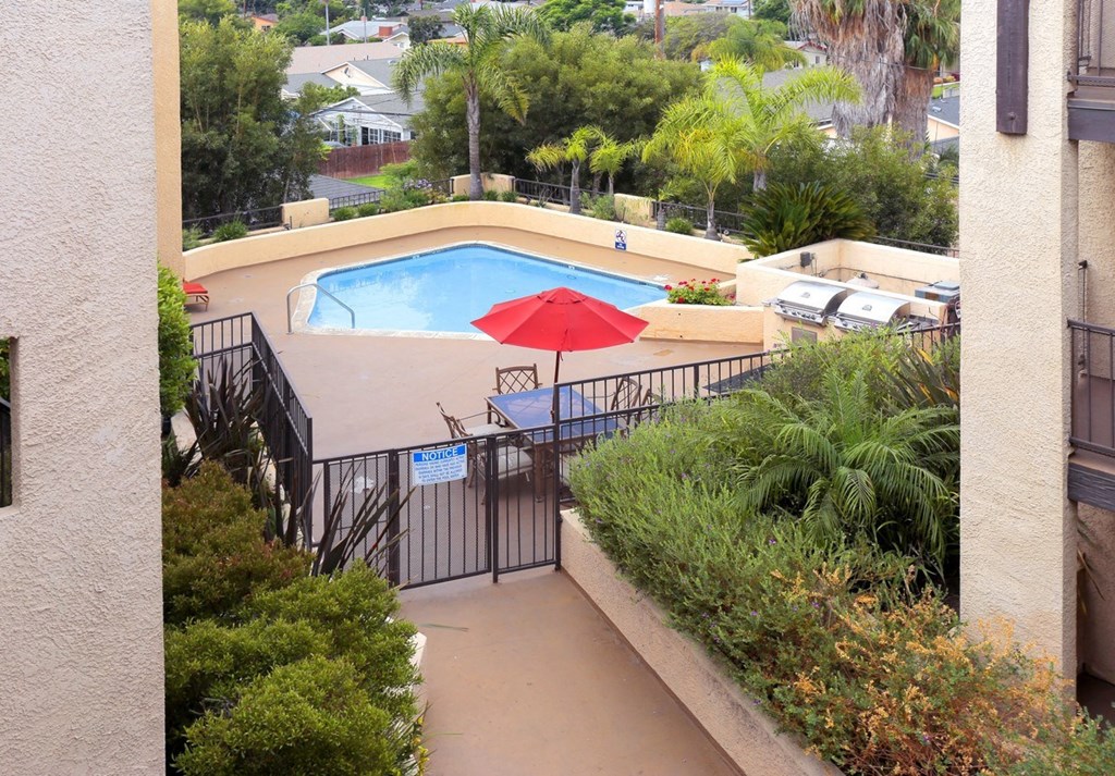 a view of a pool from a balcony with a red umbrella
