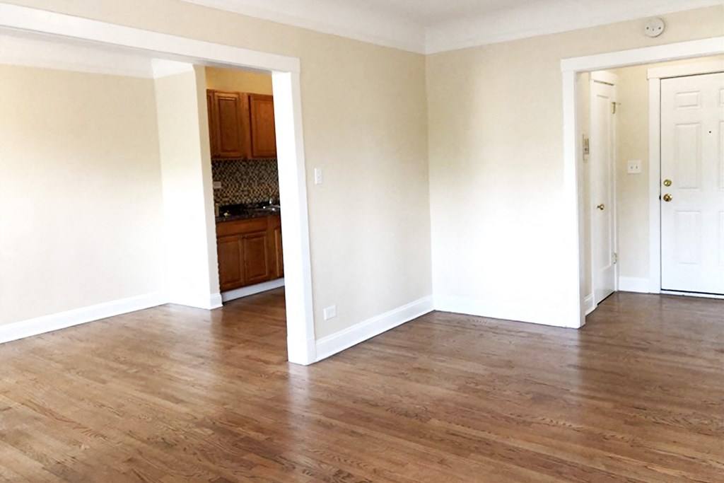 an empty living room with hardwood floors and a kitchen in the background