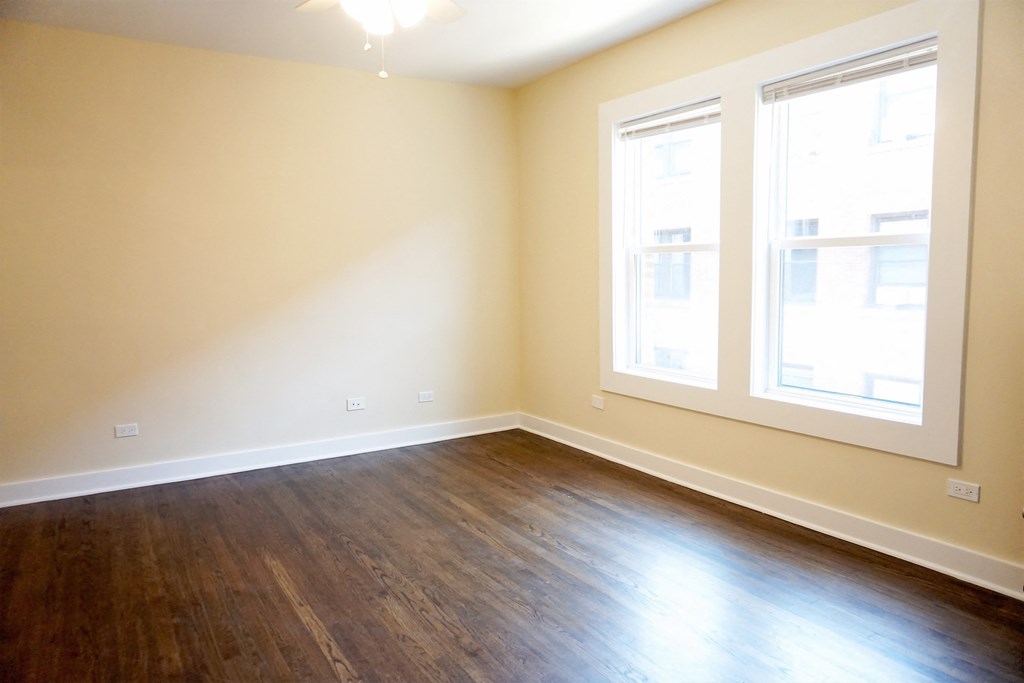 an empty room with wood floors and two windows