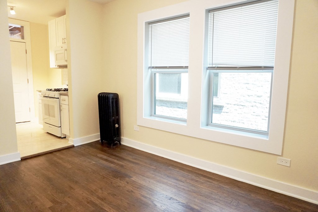an empty living room with two large windows and a stove in the background