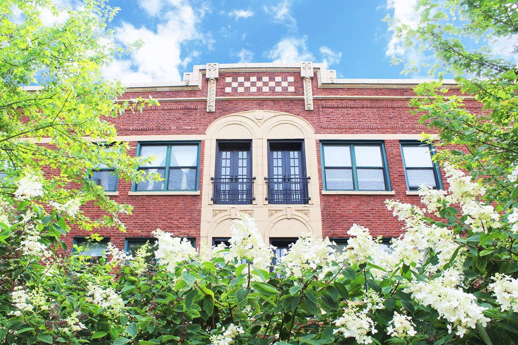 the front of a brick building with trees and flowers