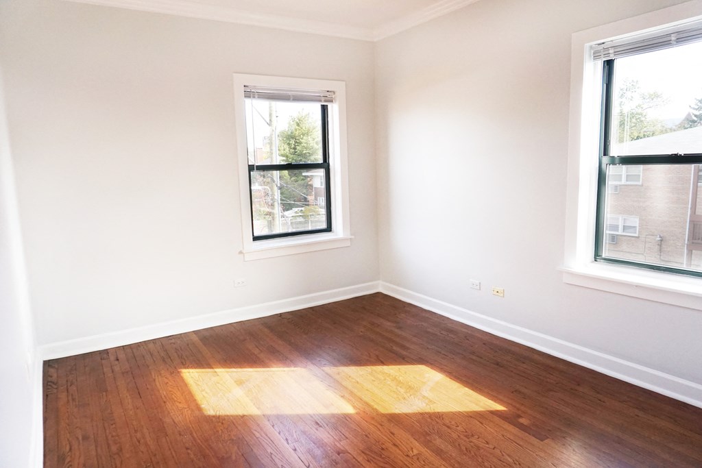 an empty room with wooden floors and two windows