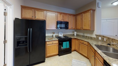 A black refrigerator is in a kitchen with wooden cabinets.