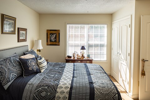 A bedroom with a large bed and a window with blinds.