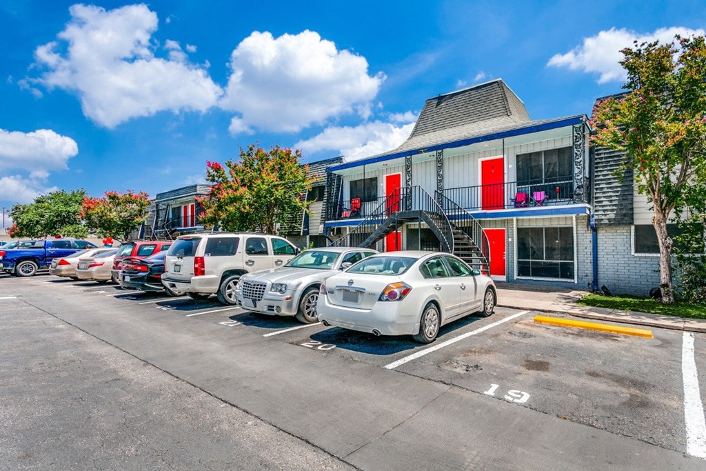 A parking lot with cars and a building with red doors in the background.