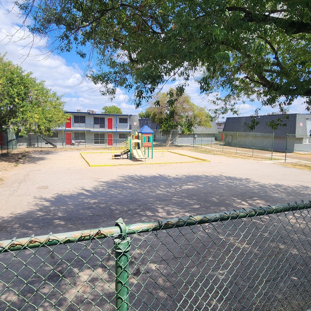 A playground with a green fence and a red and grey building in the background.