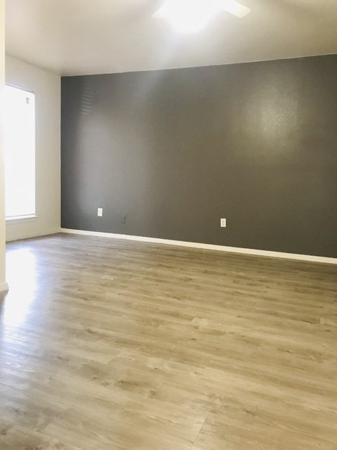 an empty living room with a gray wall and wood floors