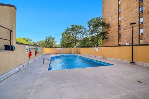 A small pool surrounded by a concrete floor and a building.