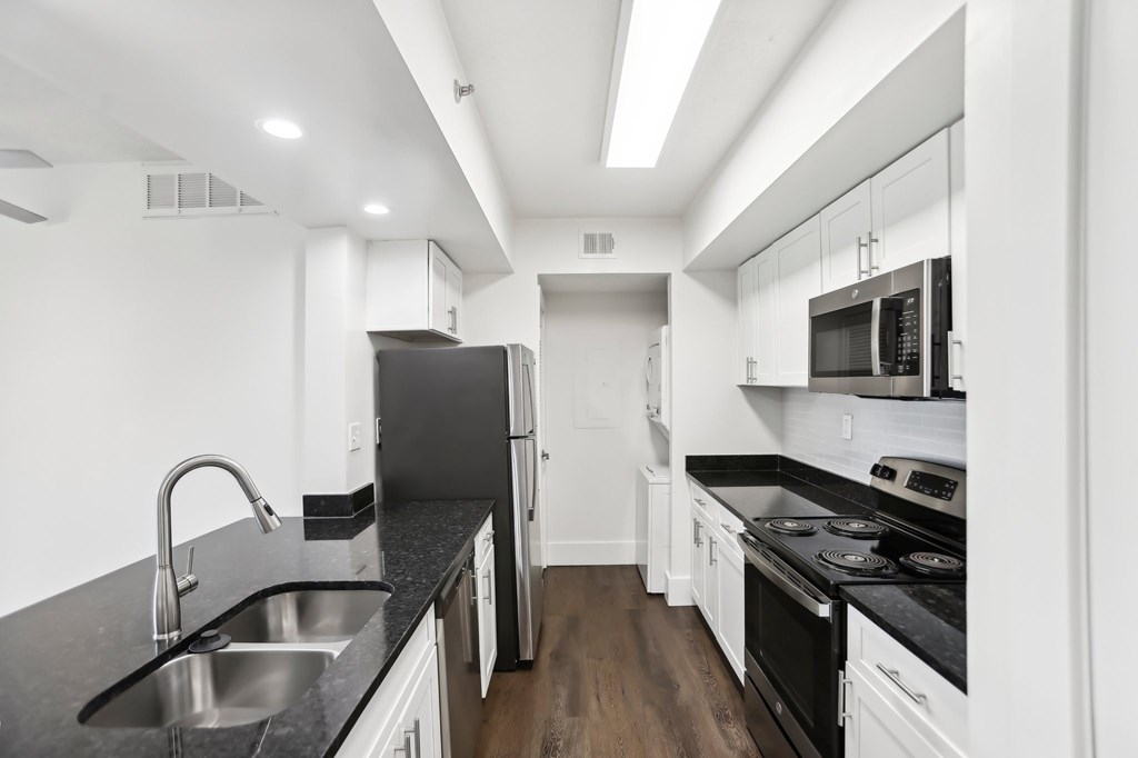 A modern kitchen with stainless steel appliances, black countertops and white cabinets.