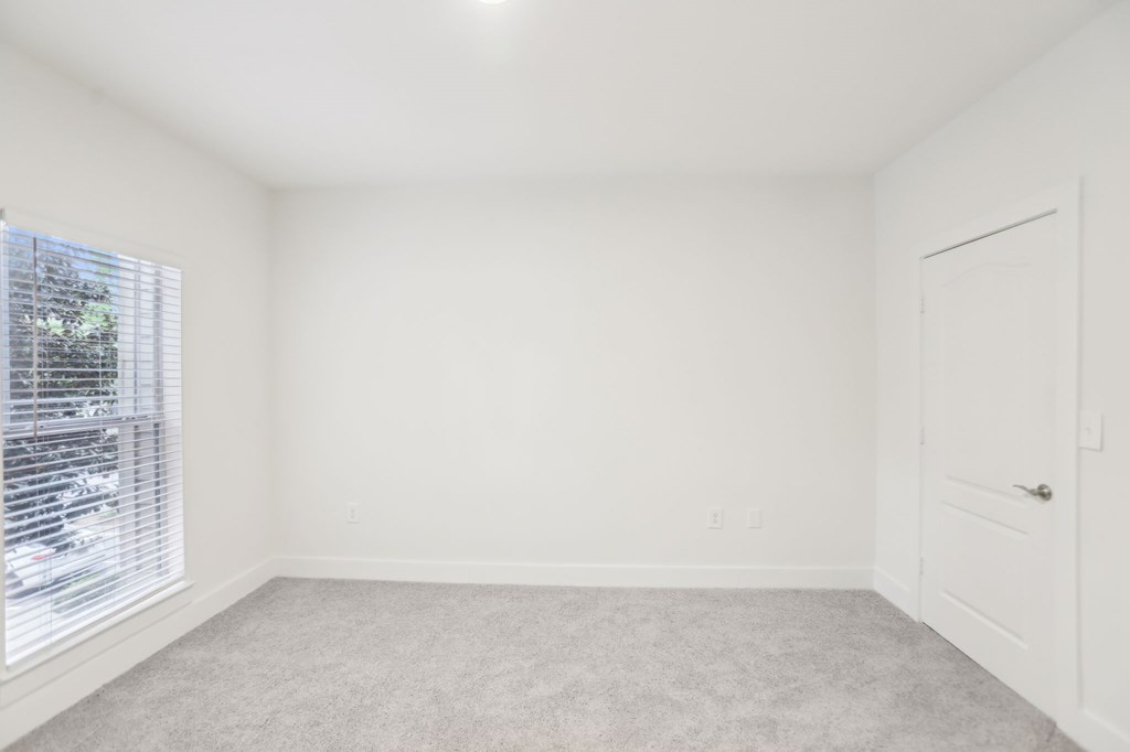 A spacious room with a carpeted floor, a window with blinds, and a closet.