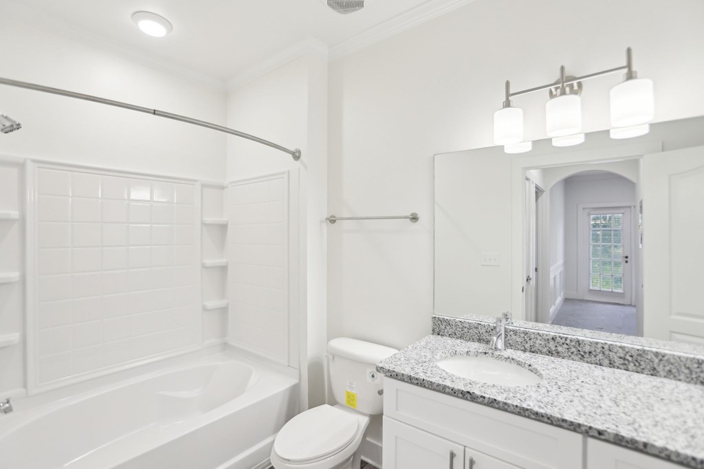 A bathroom with a tub, toilet, and granite sink.