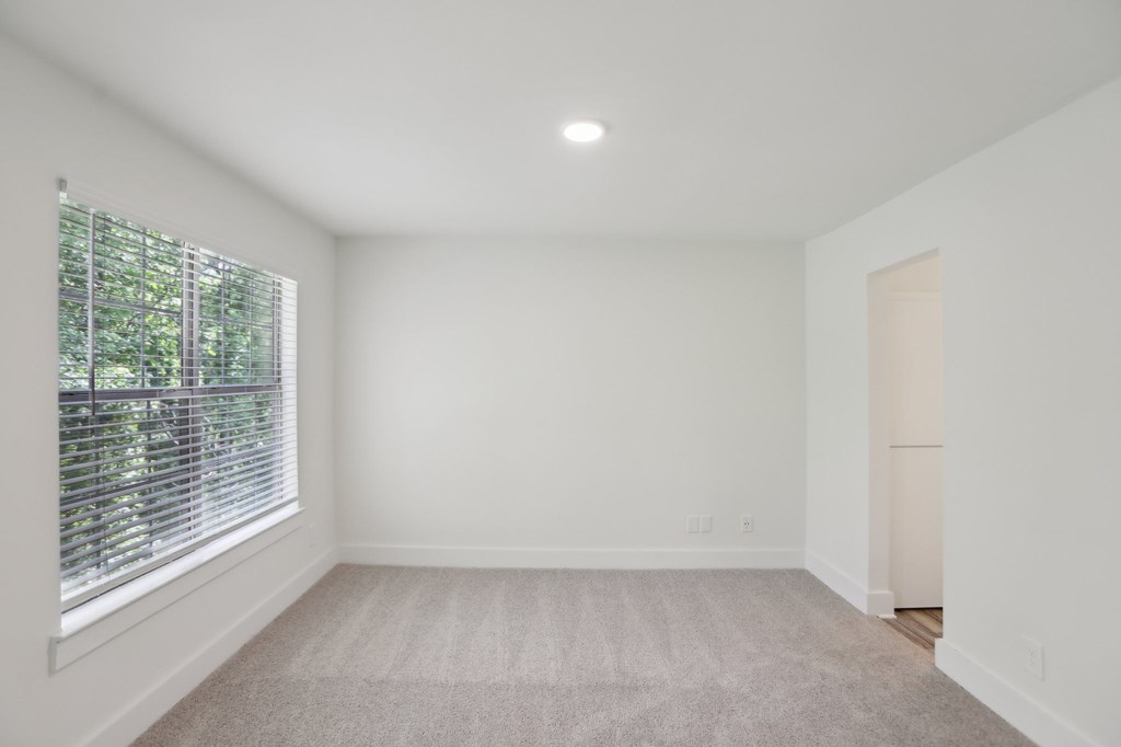 A spacious bedroom with a window and a carpeted floor.