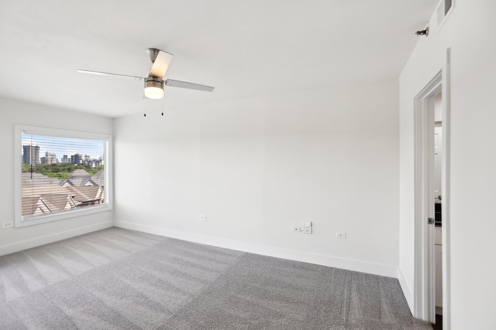 A room with a ceiling fan and a window overlooking a cityscape.