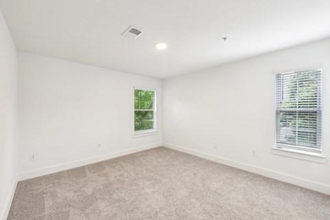 A room with a carpeted floor and two windows.