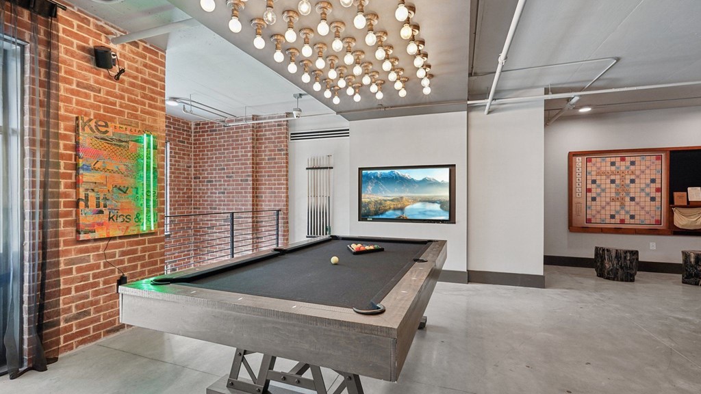 A pool table is in the middle of a room with a brick wall and large TV