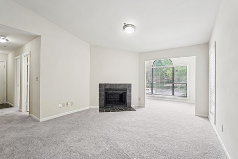 A spacious living room with a fireplace and a window overlooking a fence.