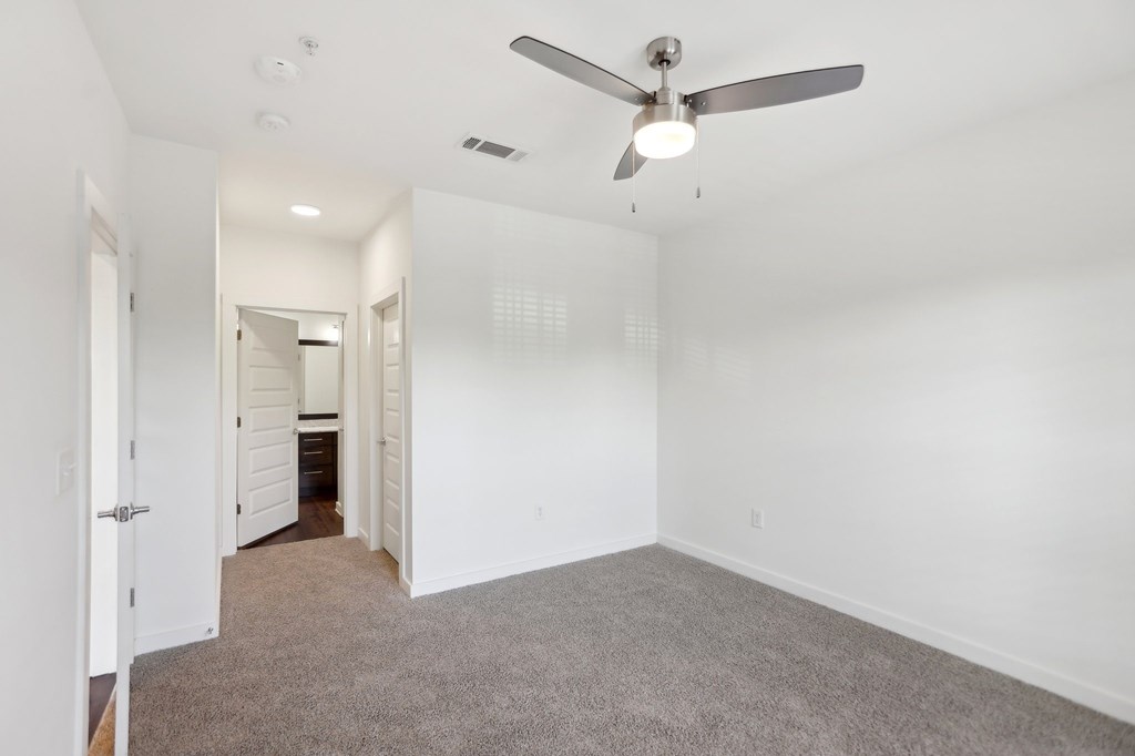 A bedroom with a ceiling fan and carpeted floor.