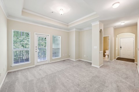 A spacious living room with vaulted ceilings,  a carpeted floor, large windows,  and a artwork niches.
