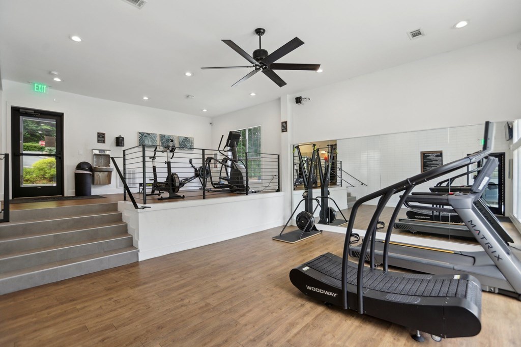 A gym with a treadmills, equipment, a staircase, and a ceiling fan.