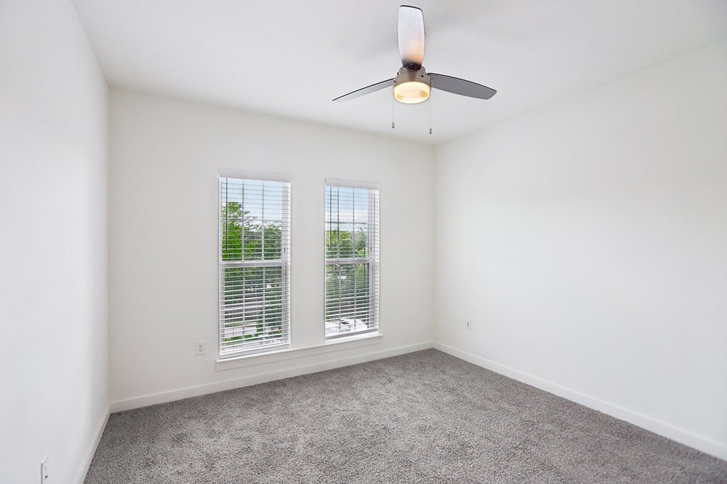 A bedroom with a ceiling fan and two windows.