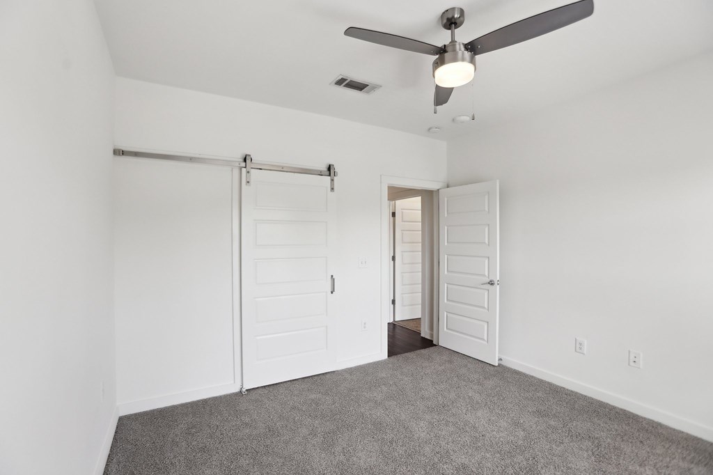 A bedroom with a ceiling fan and barn door closet.