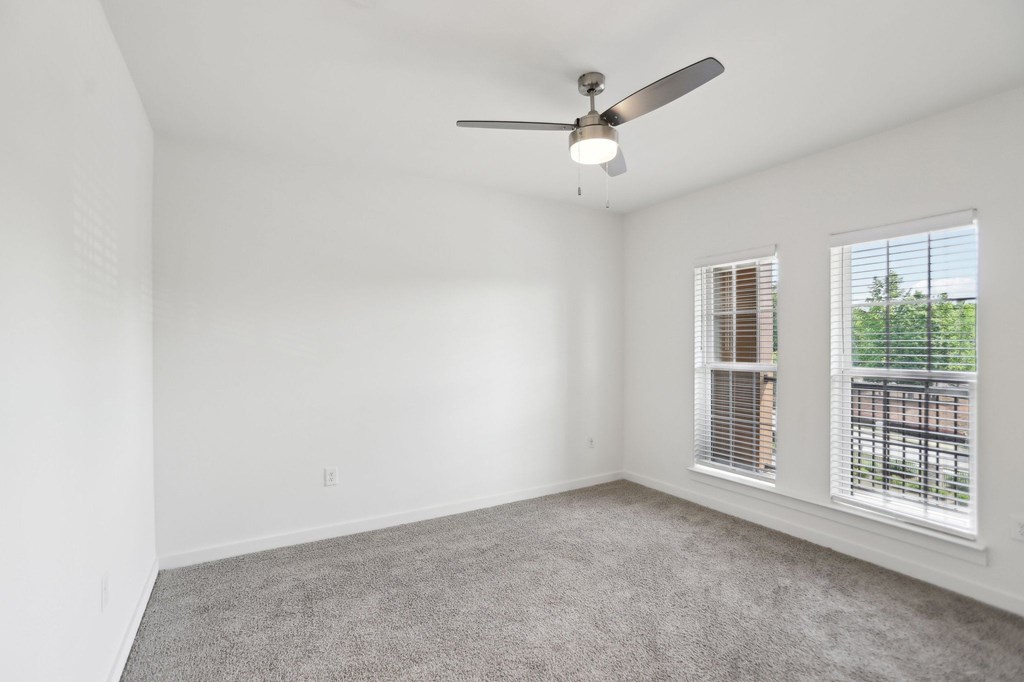 A large bedroom with a ceiling fan, windows, and carpeted floor.
