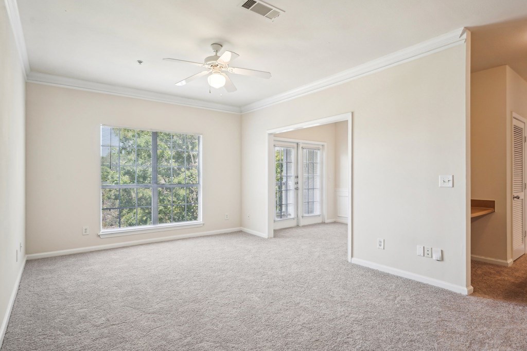 A spacious living room with a ceiling fan, carpeted floor and windows.