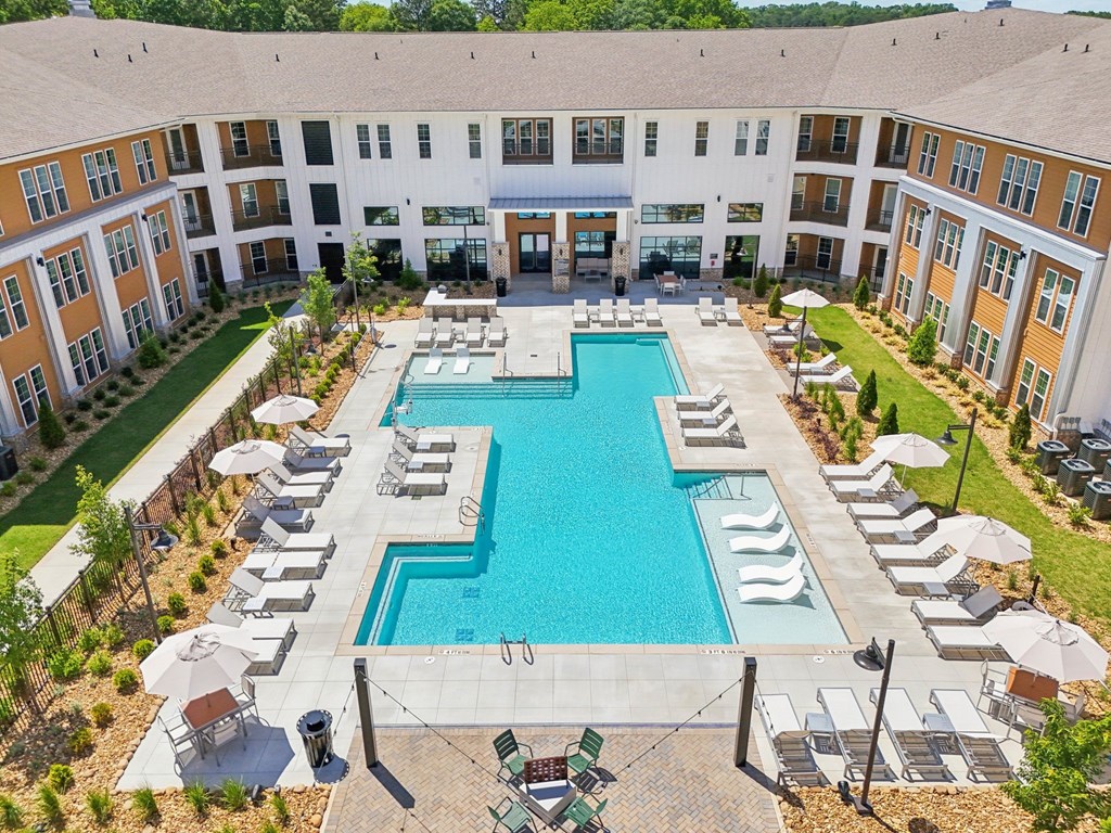 A large swimming pool surrounded by lounge chairs and umbrellas in a courtyard.