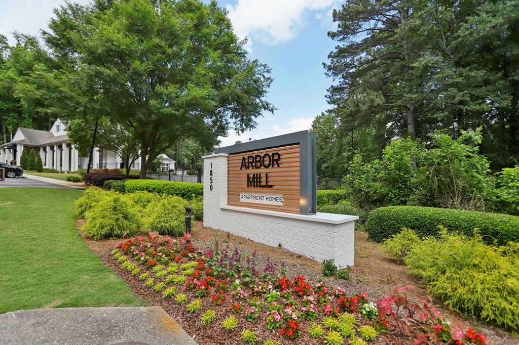 A sign for Arbor Mill is surrounded by flowers and greenery.