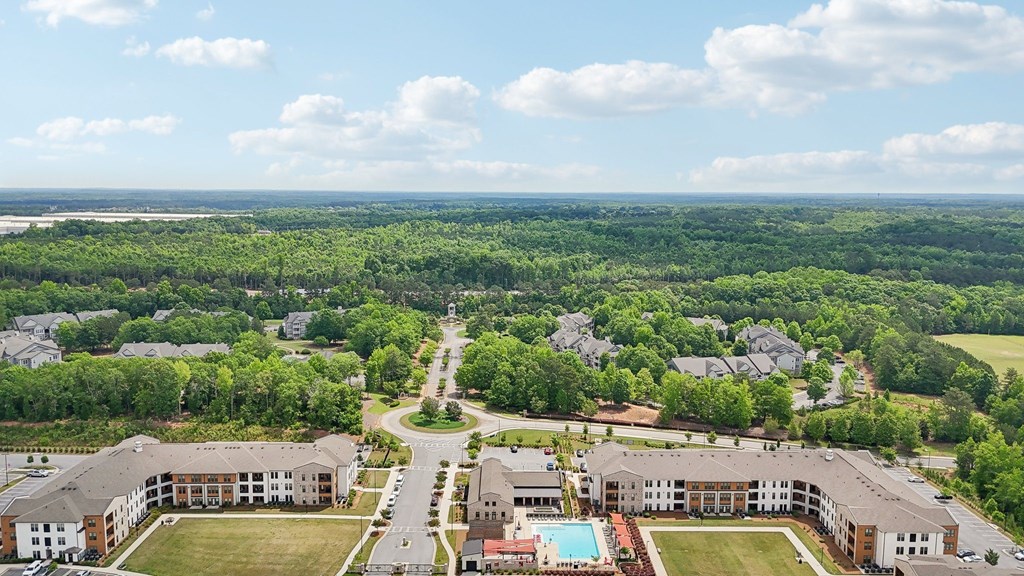 aerial view of the apartment complex with the pool ad many trees in view with beautiful skies