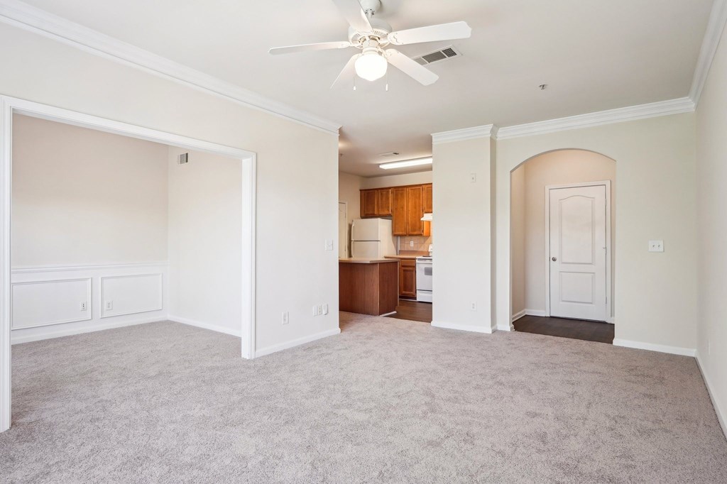 A spacious  living room with a ceiling fan and carpeted floor.