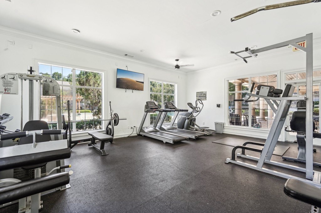 A spacious gym with various exercise equipment and a view of the outdoors through the windows.
