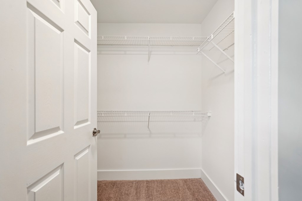 A white door is open to a room with a white wall and a brown carpet.