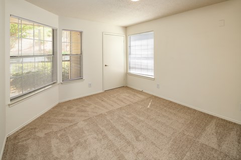 A room with a carpeted floor, a door, and a window with blinds.