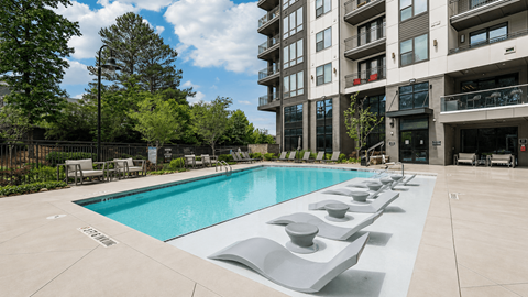 A large swimming pool with lounge chairs and apartment buildings in the background.