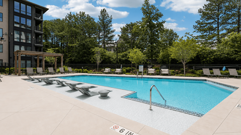 A large outdoor swimming pool with lounge chairs and a building in the background.