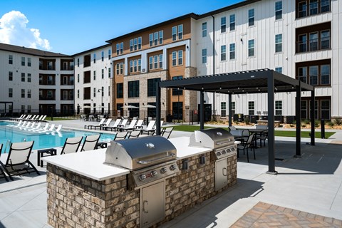 A large outdoor grill is in front of a building with a pool.