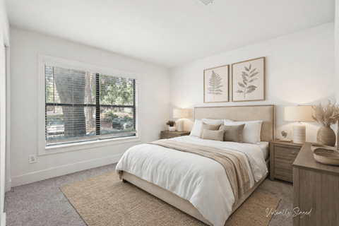 A bedroom with a large bed, a window with blinds, and a wall-mounted light fixture.
