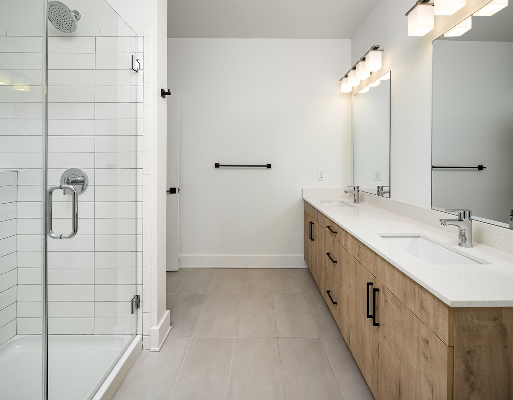 A white tiled bathroom with a walk-in shower and double sink vanity.