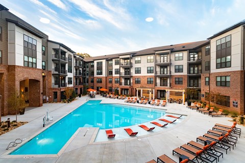 A large swimming pool surrounded by red lounge chairs and apartment buildings.