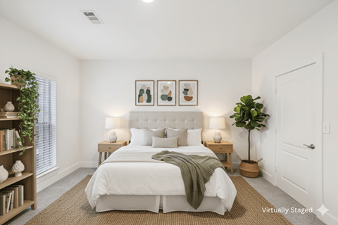 A bedroom with a large bed, a nightstand with lamps, a plant, and pictures on the wall.