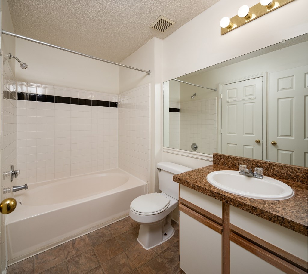 A white bathroom with a brown granite counter top.